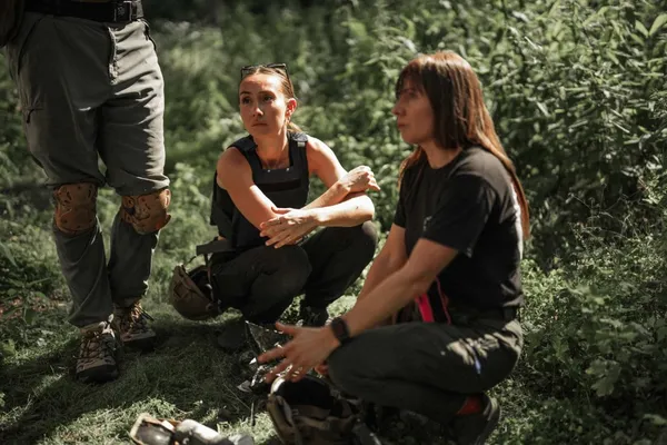 Two people crouch in woodland during a Daily Humanity travel-safety training exercise.